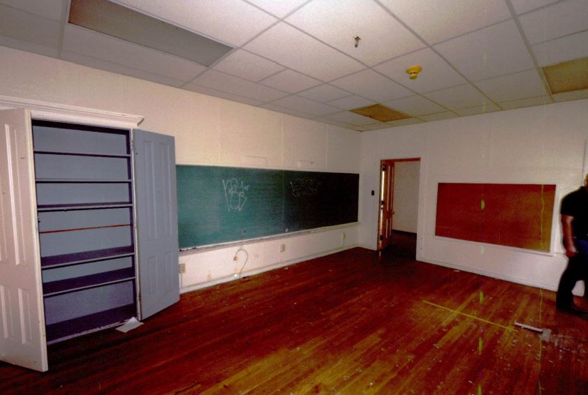 Room with wood floor, chalkboard, cabinet and doors.