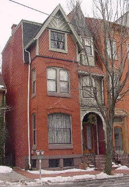 Small brick rowhouse with tree in front.
