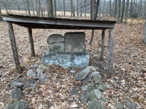 Low wood shelter over gravestones in wood.