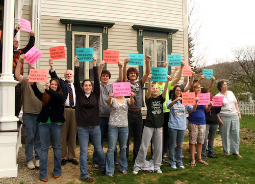 This photograph shows a group of people holding signs in front of an old house.
