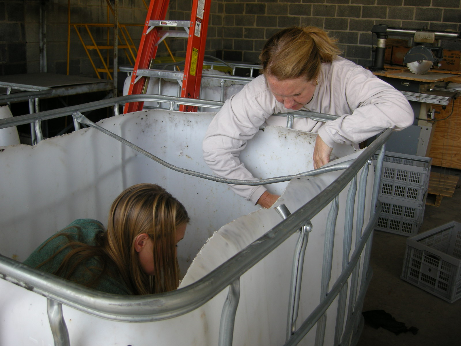 This photograph shows two people working in a large bin.