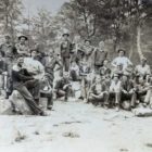 Large group of men standing in forest.