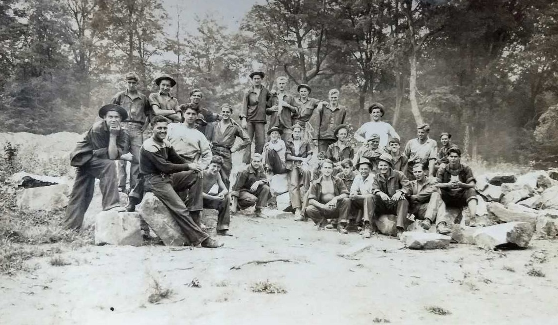 Large group of men standing in forest.