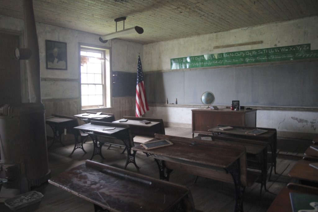 Inside an old one-room school with desks and chalkboard.