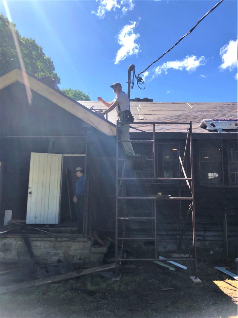 Man working on roof of wood building.