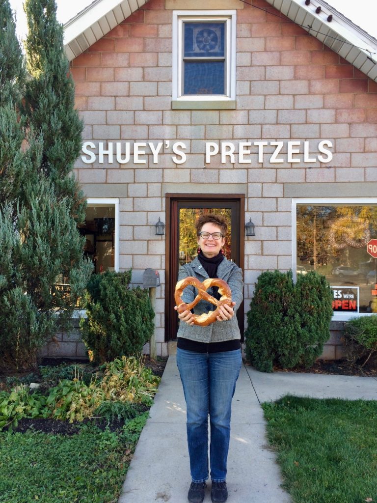 Woman standing in front of building holding a large pretzel.