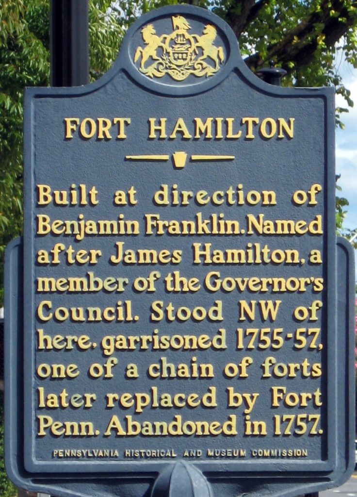 Blue metal sign with gold lettering about Fort Hamilton site.