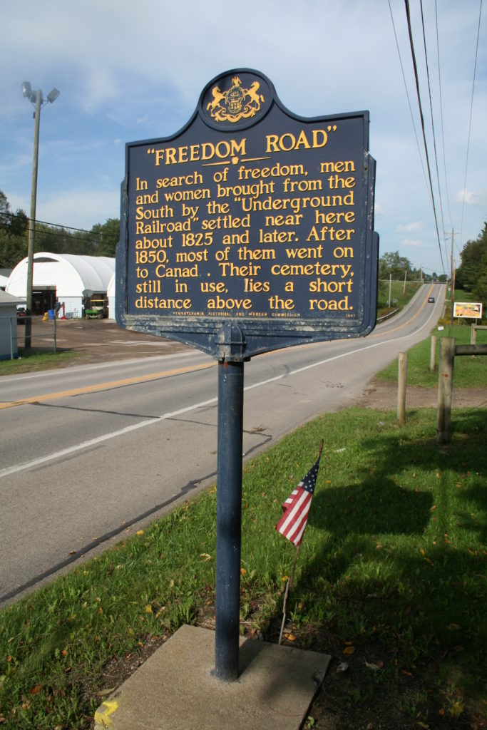 Large blue metal sign on a tall blue metal post with yellow writing for "Freedom Road" in Mercer County, PA