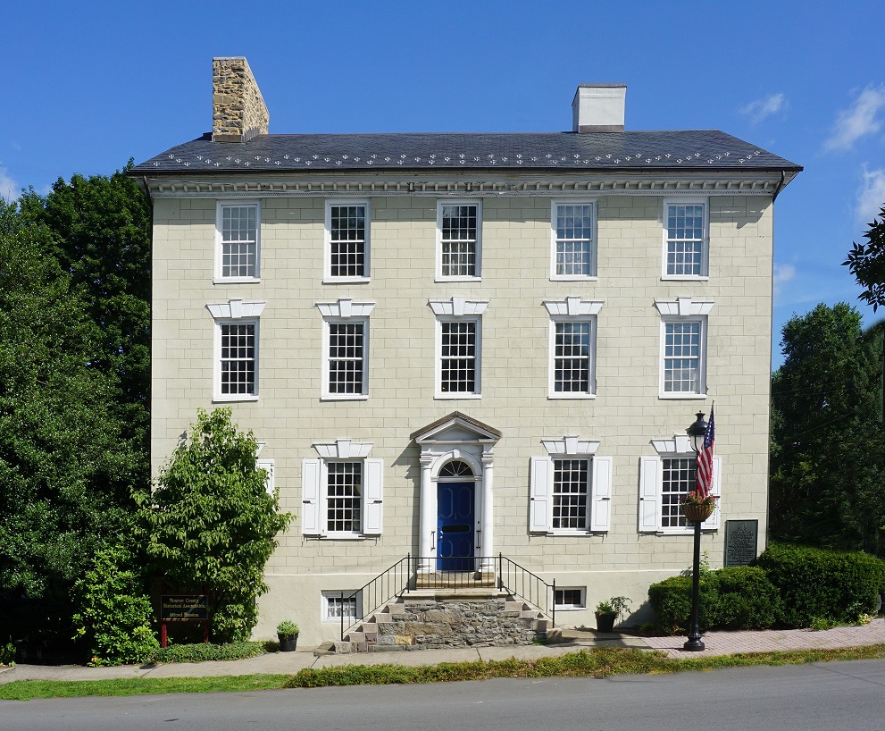 Large three-story, five-bay stone buildings with white windows and blue door.