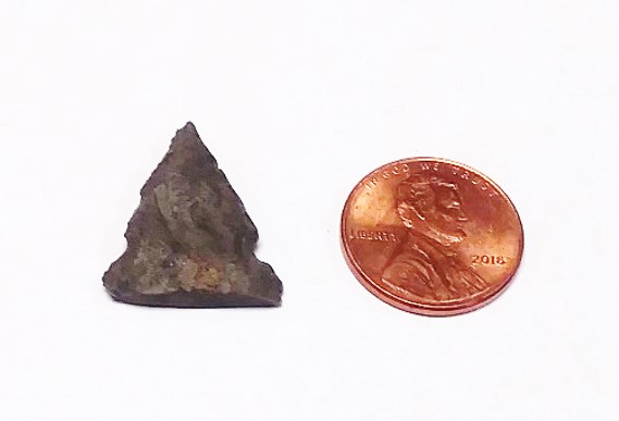 A stone point next to a copper U.S. penny.