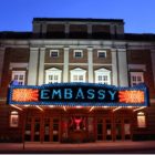 Brick theatre building with marquee that spells "Embassy" in lightbulbs.