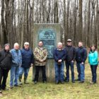 Group of people standing in clearing next to tall stone marker
