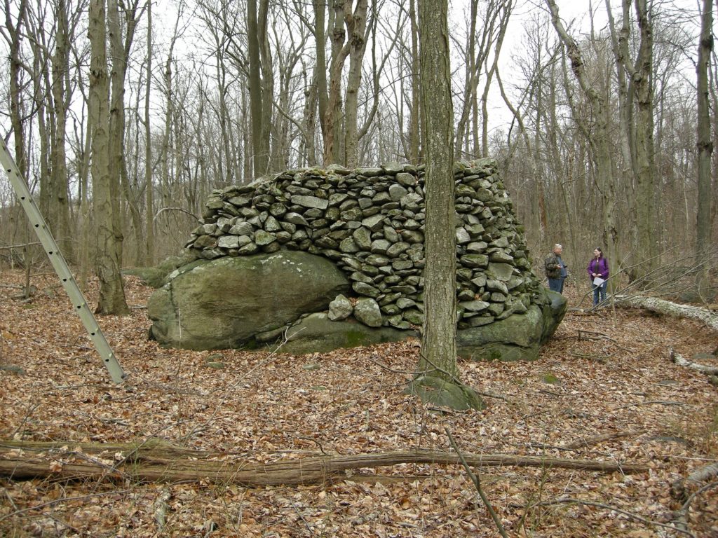 Large pile of small stones around a large boulder in woods