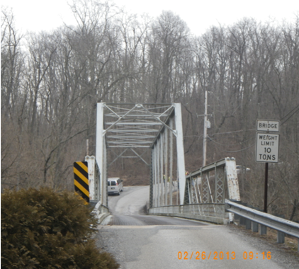 Metal truss bridge in front of bare trees.