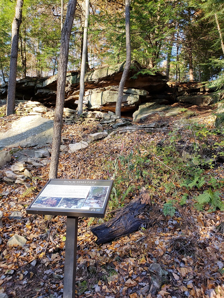 Wooded hillside with large rocks and sign on wood post.