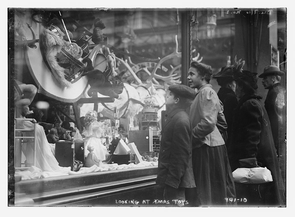 Black and white photograph of woman with boy looking at toys through large plate glass window.