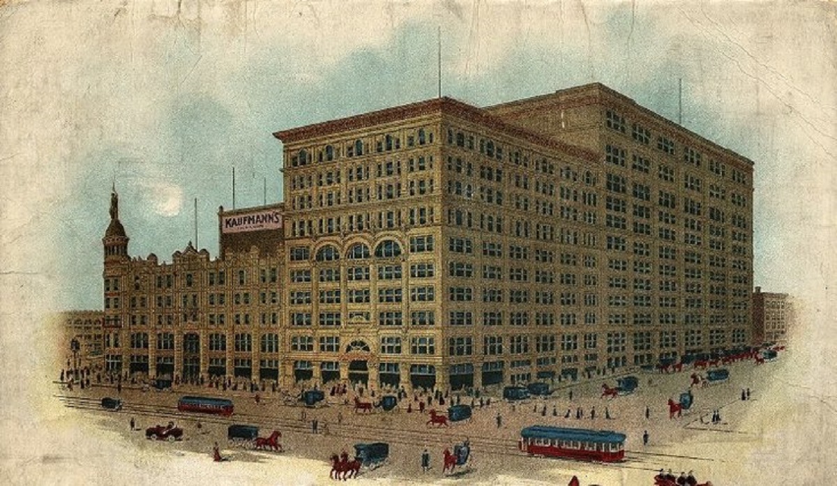 Colorized historic postcard of large department store with trolleys, horses, carts, and people in the foreground.
