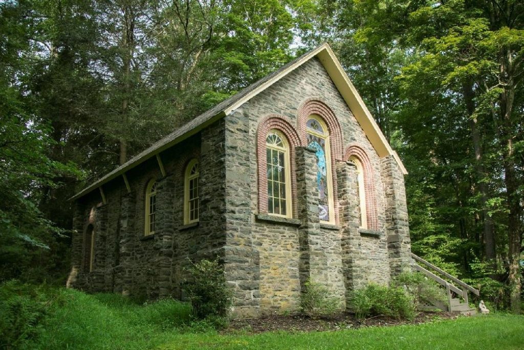 Small stone chapel with arched windows set in wooded area.