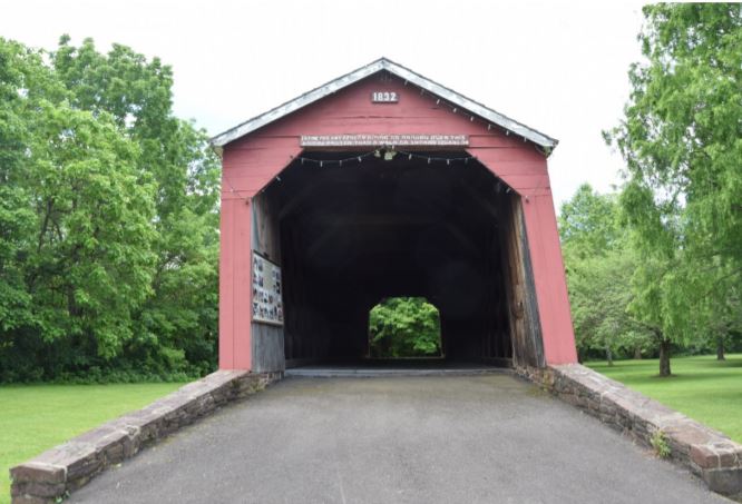 Wooden covered bridge surrounded by lawn and trees.