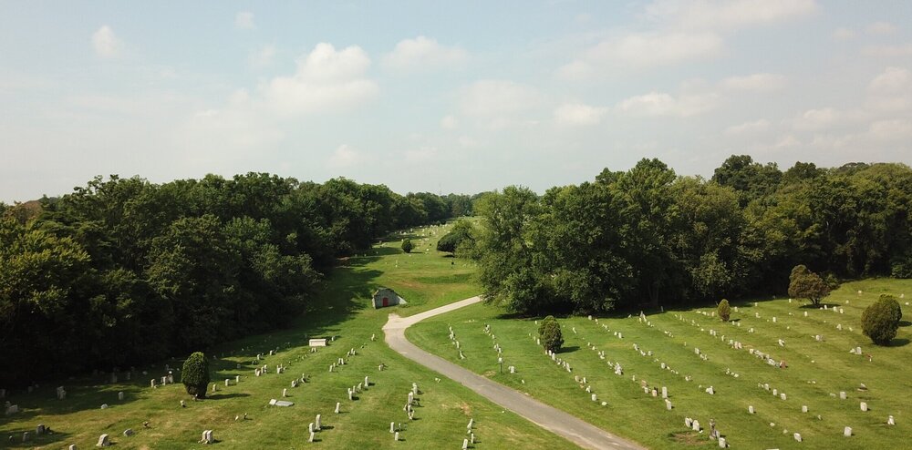 Looking across a cemetery with mature trees, grave markers, lawns and a path.