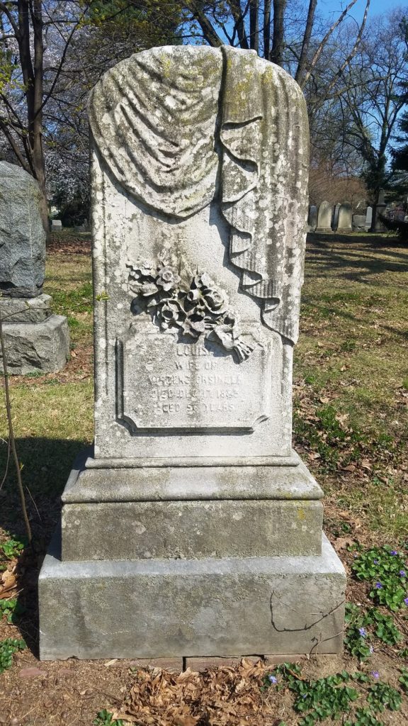 Stone grave marker carved with cloth draped over top and flowers.