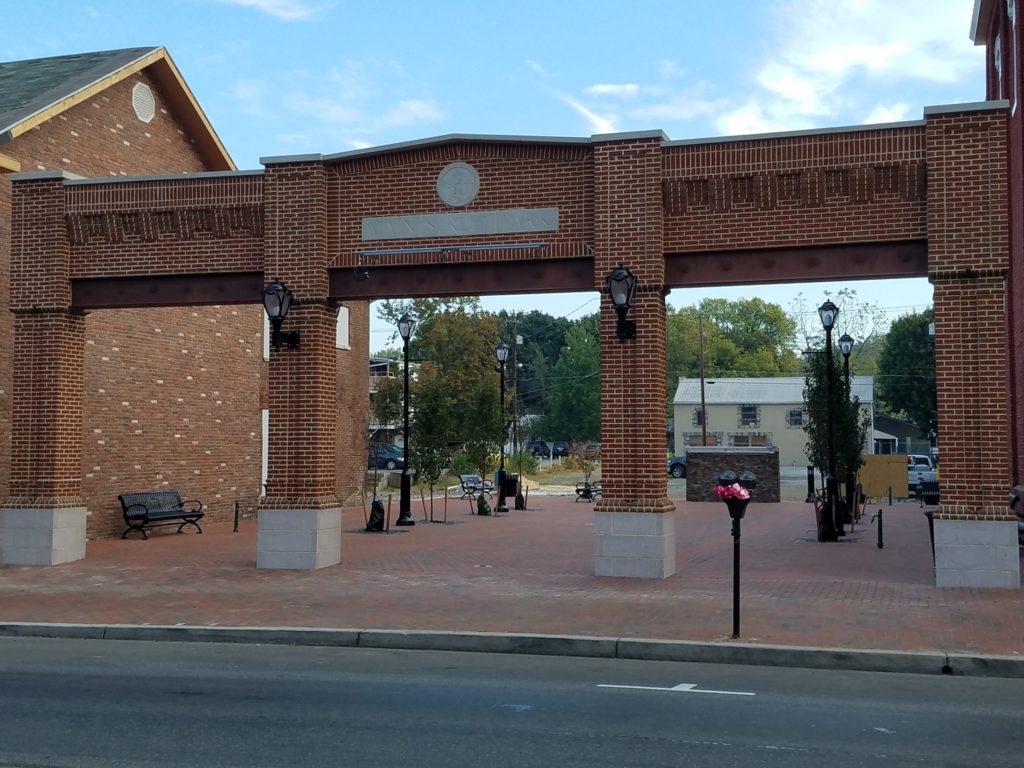 Brick building facade with large openings in front of brick paved plaza.