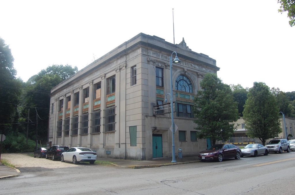 Large rectangular stone building with large windows along the side and front facades along a wide street.