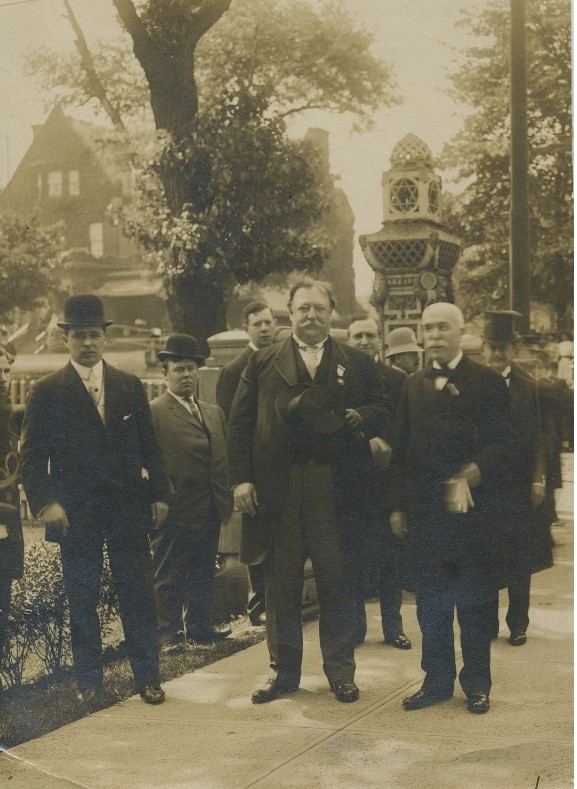 Historic photograph showing a group of white men standing outside on a sidewalk.