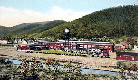 Colorized historic photograph of factory buildings along a river.
