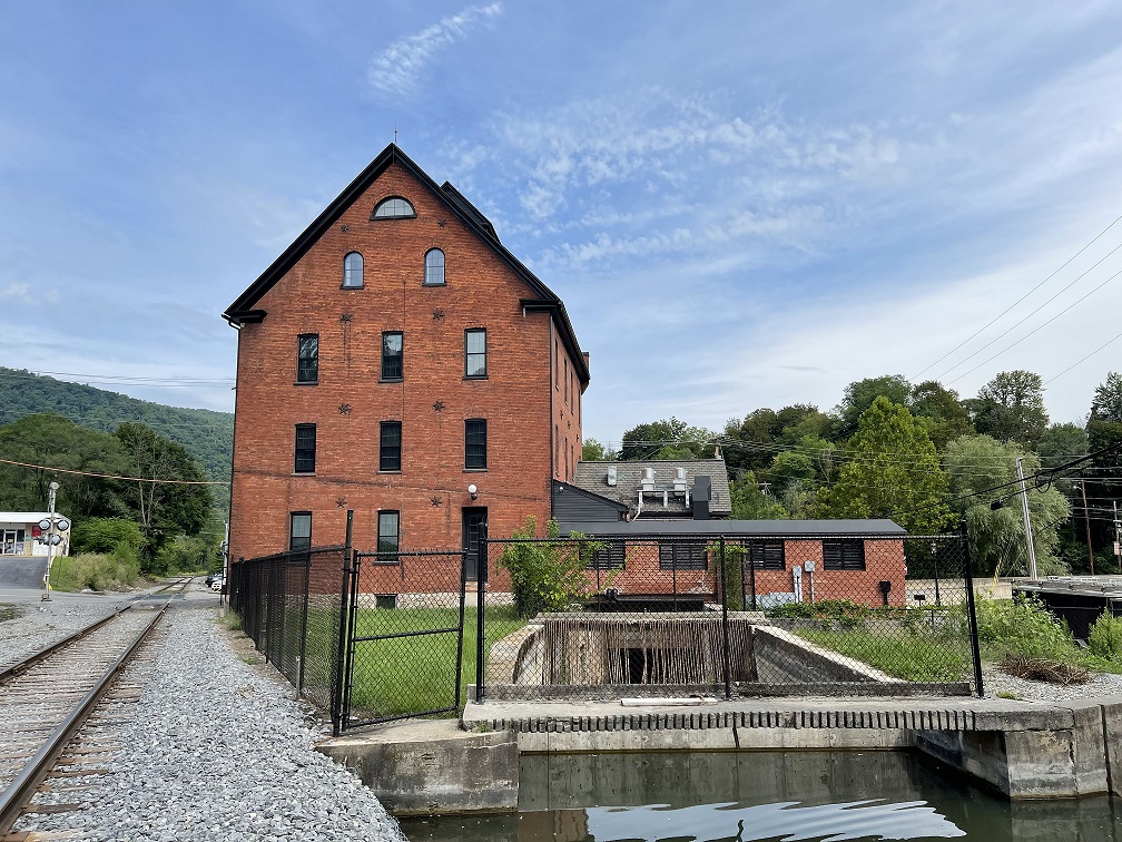Large brick building next to water surrounded by trees.