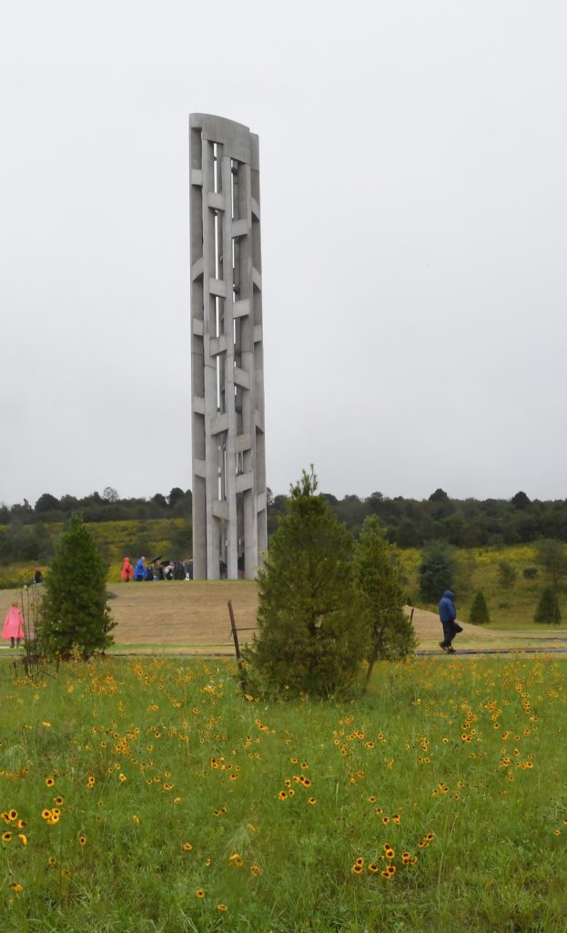 Tall stone tower in field surrounded by people.