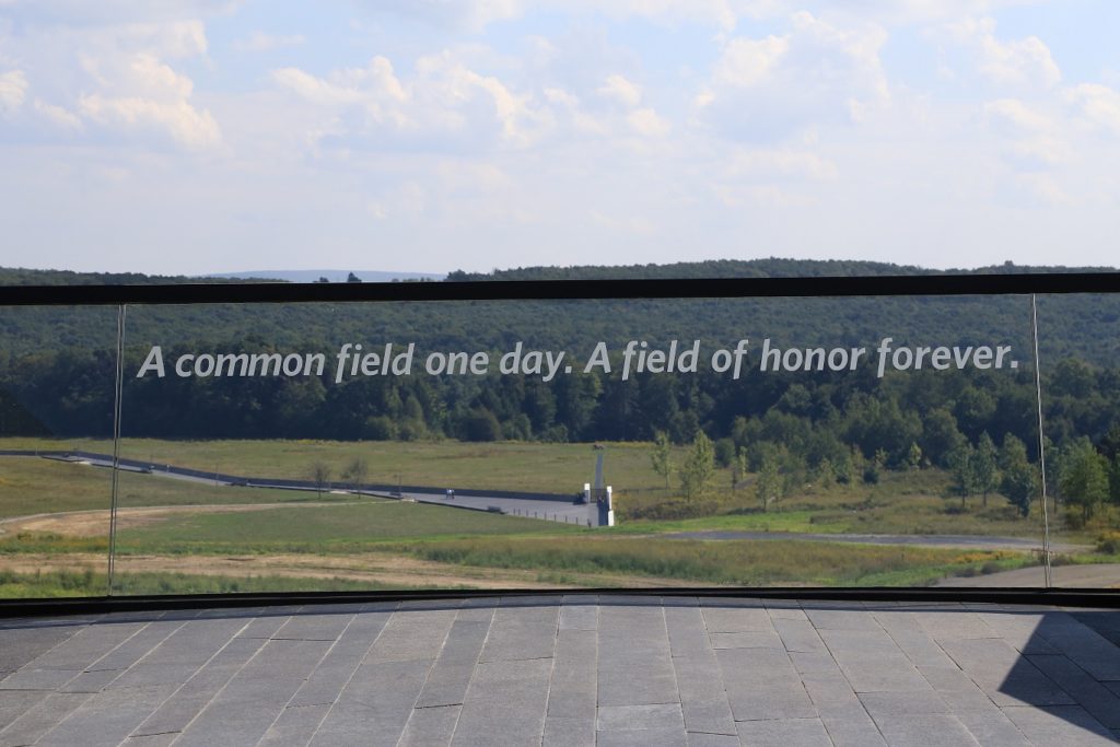 Clear window looking at a field with text "A common field one day. A field of honor forever."