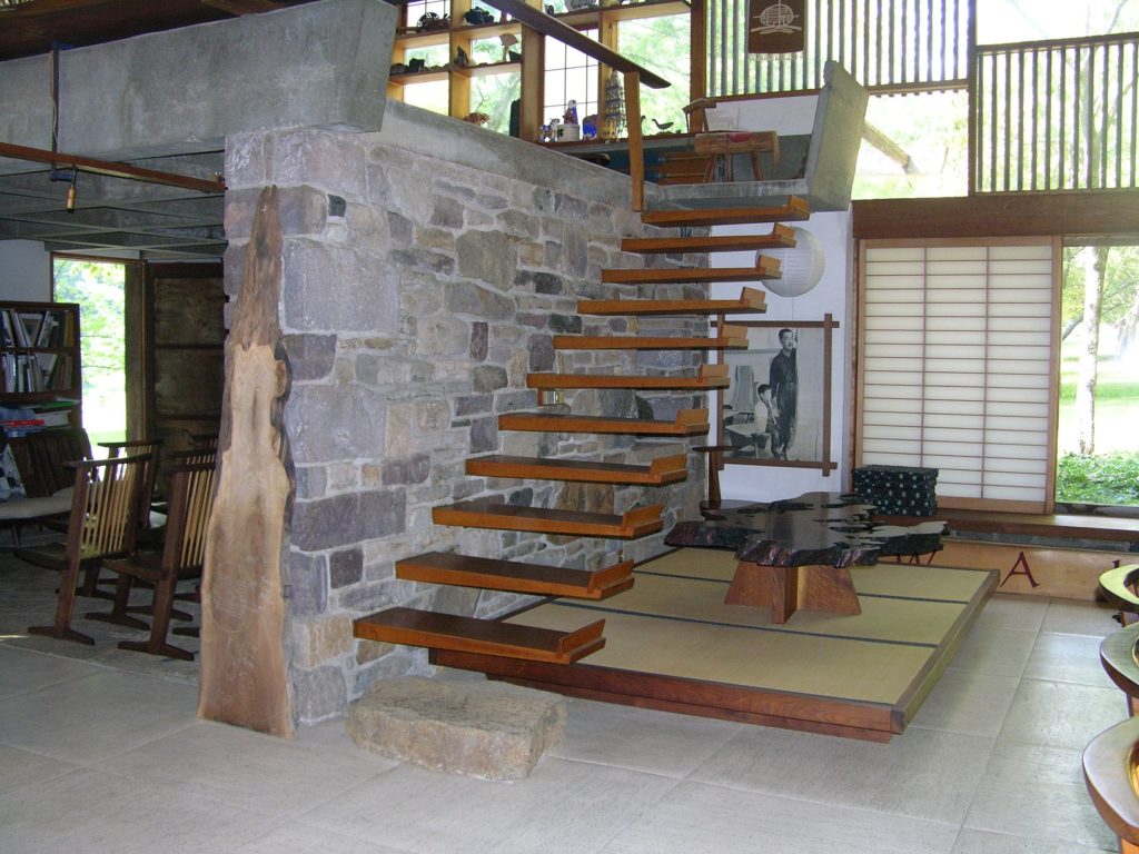 Large room with stone wall and floor, wood stair and large windows.