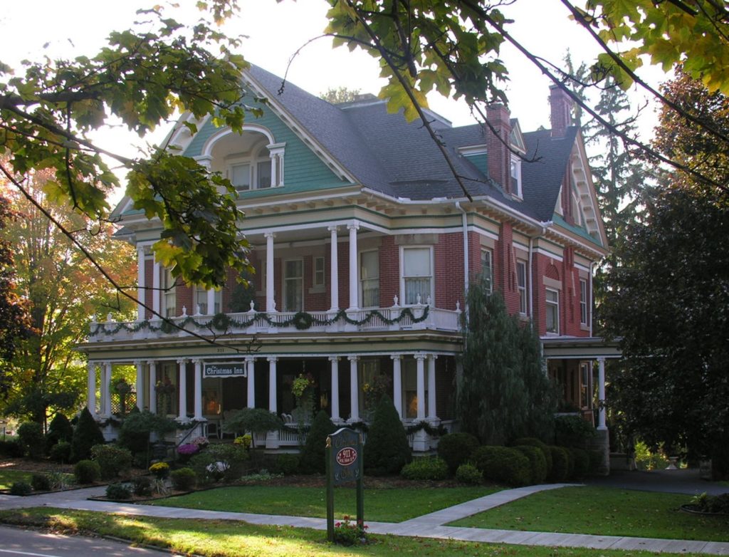 A large house with two story front porch surrounded by green lawn and trees.