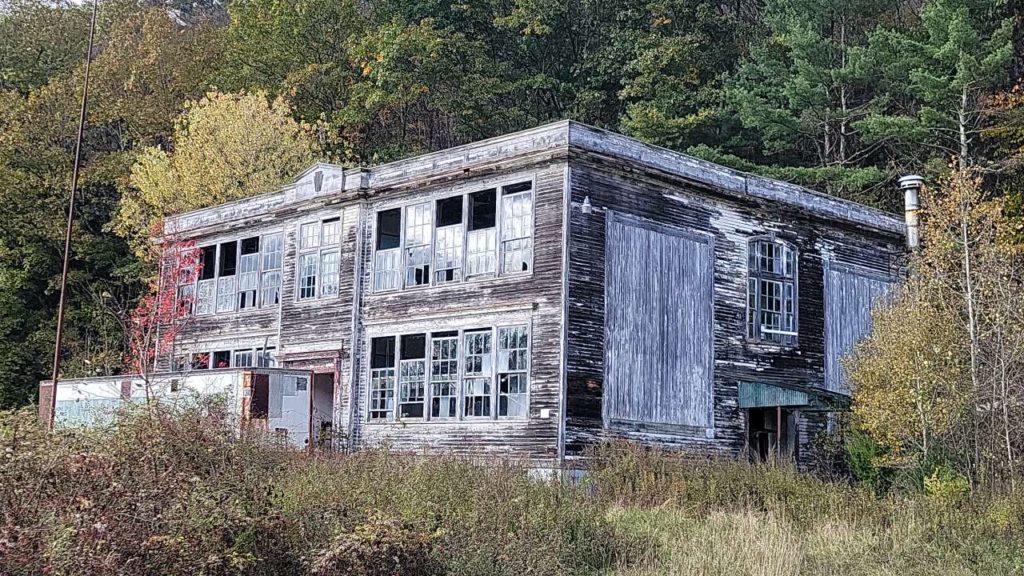 Two story wood building with broken windows in a wooded area.