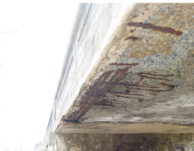 Underside of a concrete bridge with exposed steel that has rusted.