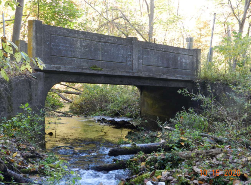 Concrete bridge over small stream in wooded area.