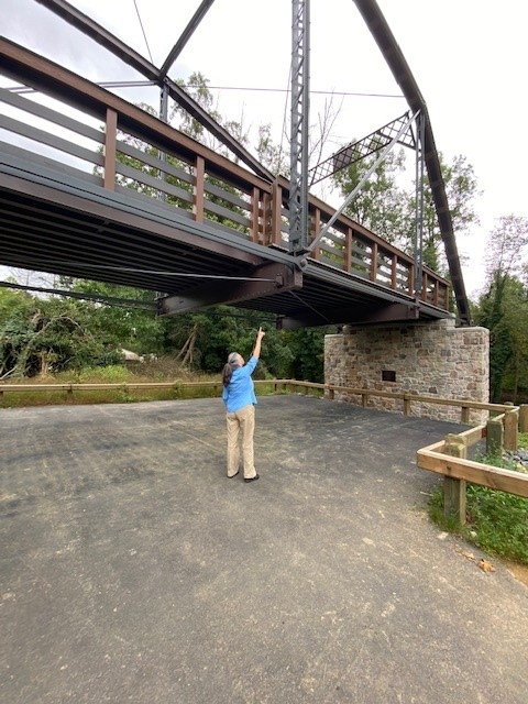 Woman standing in parking lot pointing to metal truss bridge.