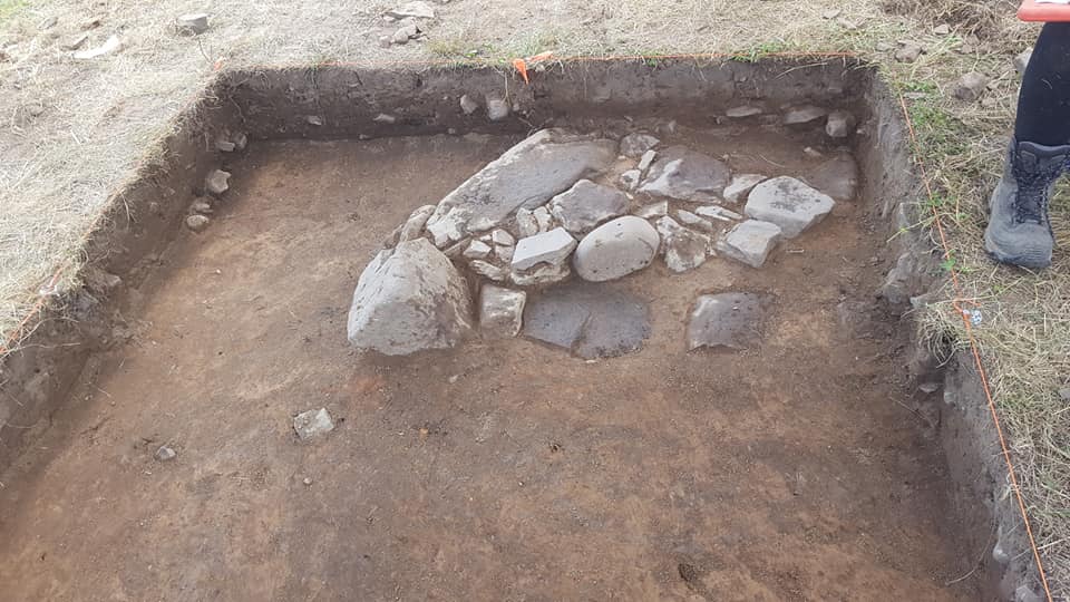 Collection of stones inside a square hole in the ground.