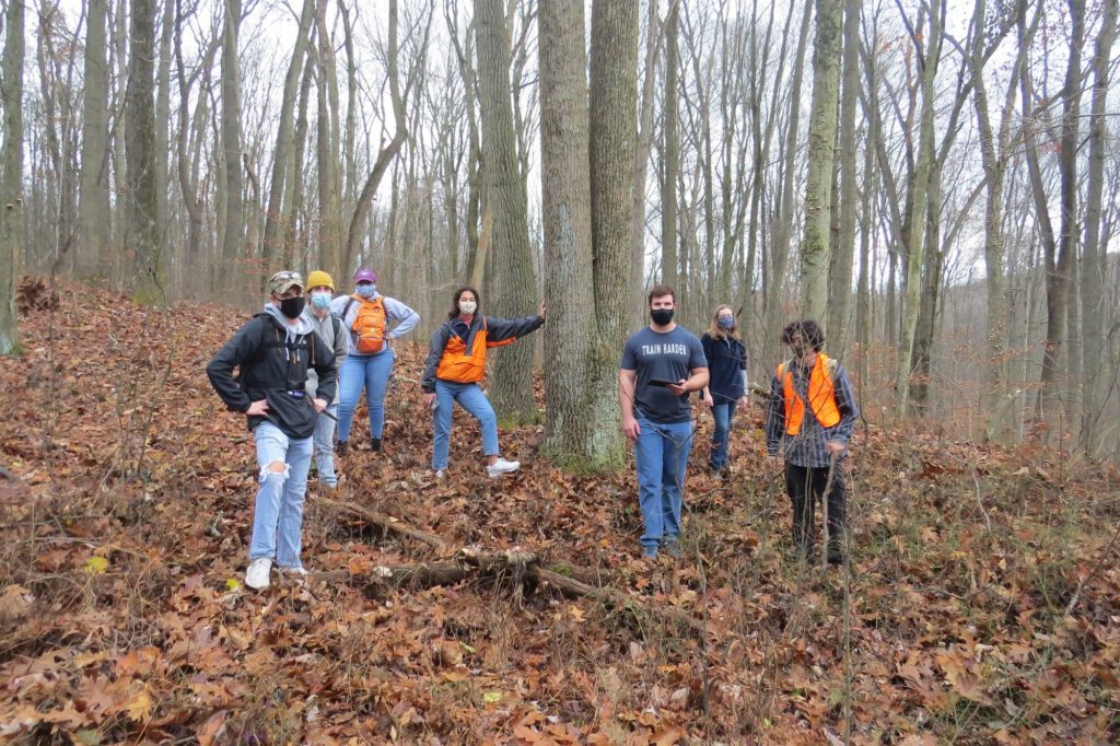 Group of seven people standing in a wooded area.