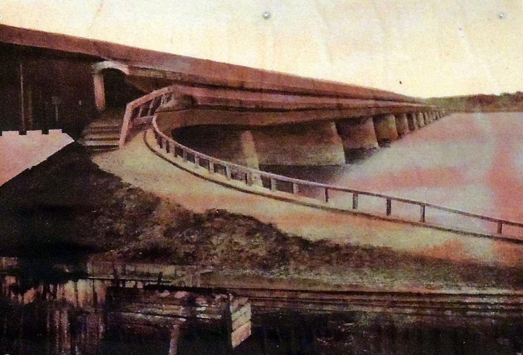 Photograph of ramp leading to wooden bridge over a body of water.