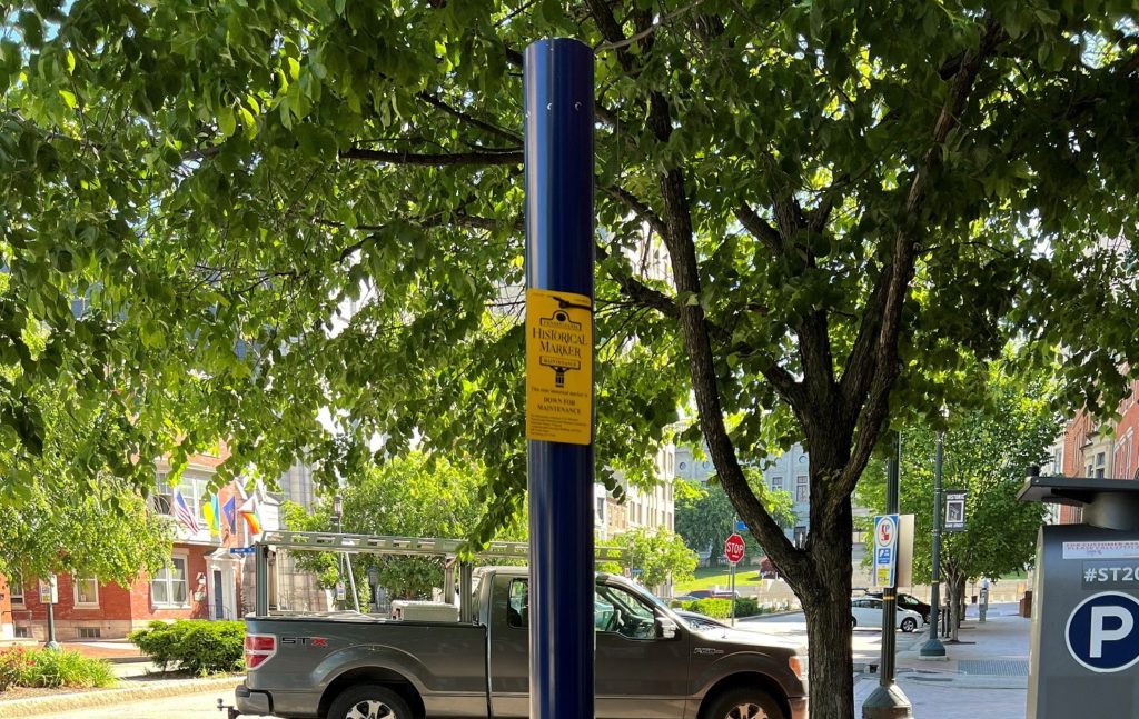 Metal pole with tag along street with trees, parked cars and sidewalks.