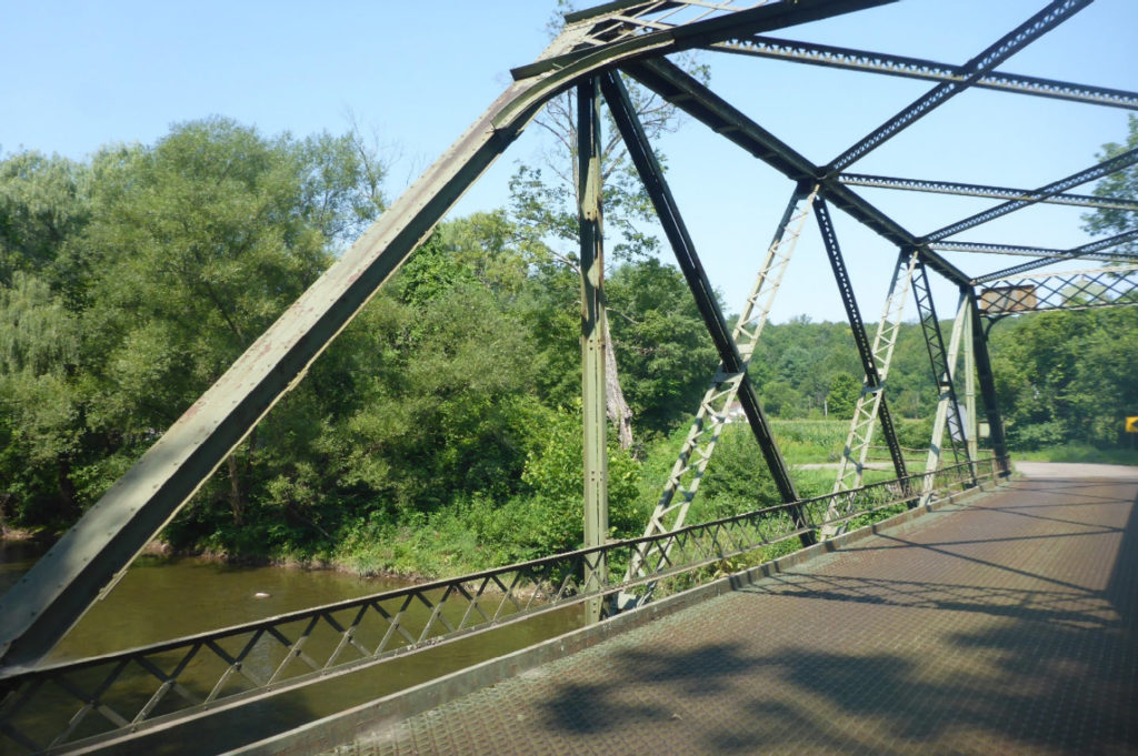 Metal trusses of a bridge over water and surrounded by trees.