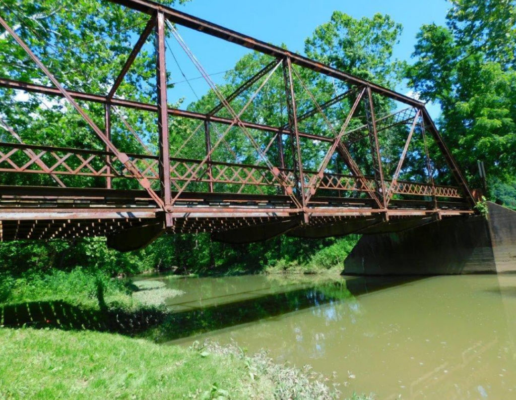 Metal truss bridge over water and surrounded by trees.