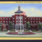 Color postcard of large brick building with landscaping in front.