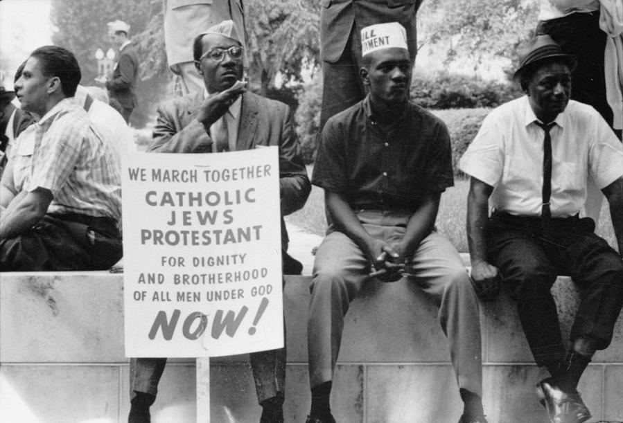 Three Black men sitting on a masonry wall with a sign.