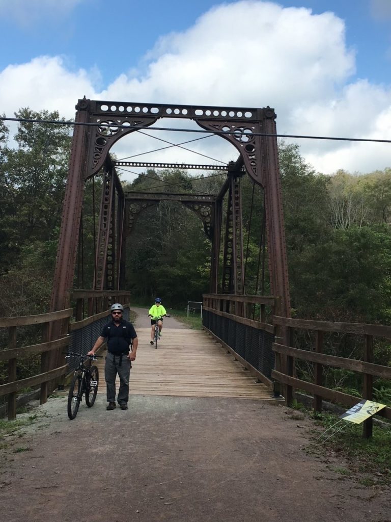 Two people riding bikes over a metal truss bridge.
