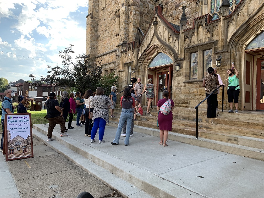 Group of people gathered on sidewalk in front of church doors.