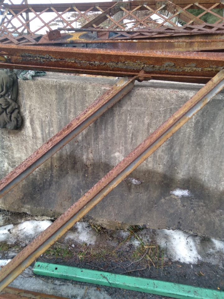 Rusted parts of the bridge's metal frame on concrete.