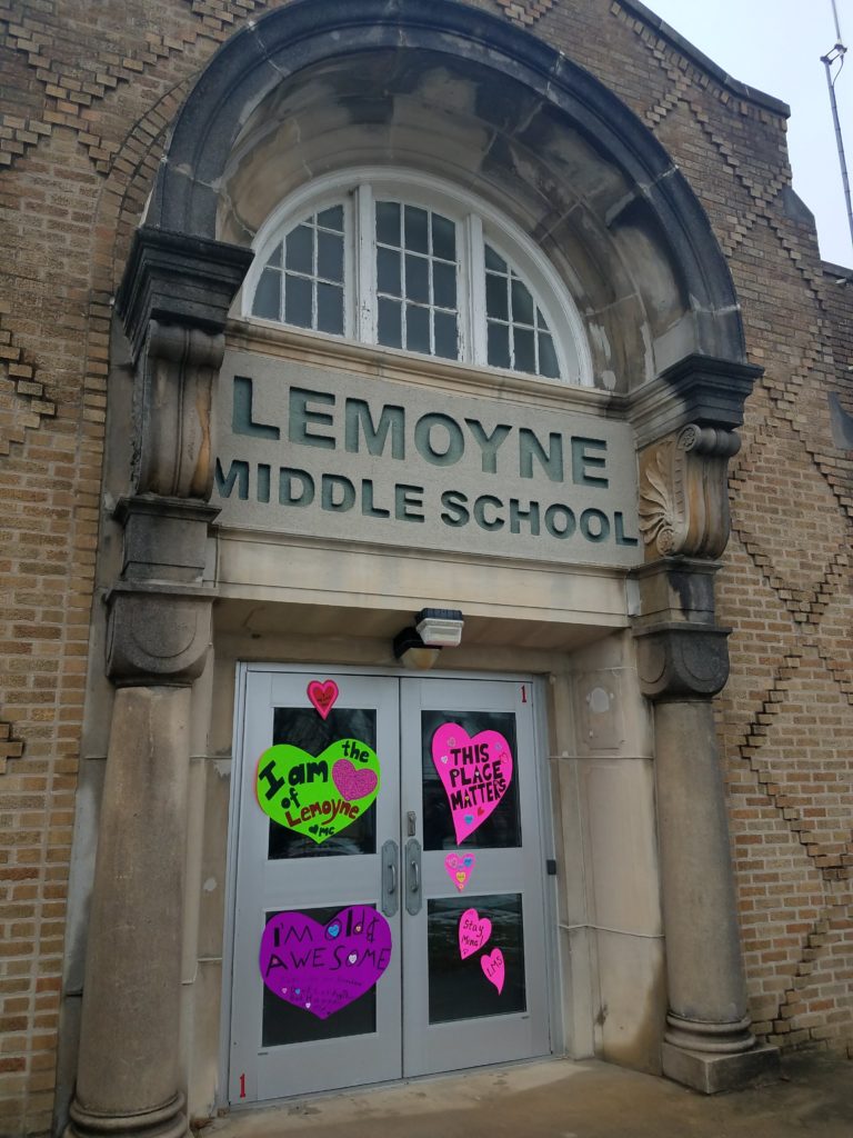 Large building entrance with metal doors and stone columns and arched window and the words "Lemoyne Middle School" above the door. Large paper hearts are on two metal entrance doors.